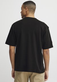 Svart bomull T-skjorte med avslappet passform, korte ermer og rund hals, sett fra baksiden. Glatt tekstur, minimalistisk design.