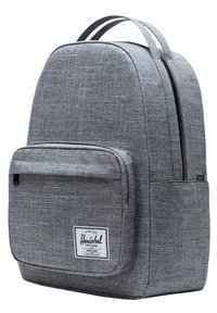 Mochila de tela gris con forma redondeada, bolsillo frontal con cremallera y una etiqueta de marca blanca. Cuenta con dos correas para los hombros y una textura suave.