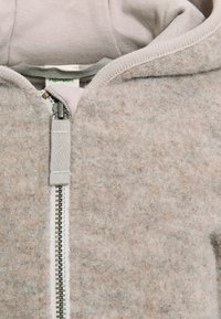 Grau gestrickter Zip-Hoodie mit einer weichen Textur, ausgestattet mit einem kontrastierenden hellgrauen Reißverschluss und einem gerippten Innenfutter der Kapuze.