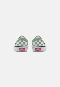 Gröna rutig canvas slip-on skor med vit gummisula och en röd logotyp patch vid hälen. Bakifrån syns detaljer med dubbel söm.
