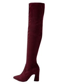 Botas burdeos que superan la rodilla en material texturizado, con punta puntiaguda y tacón grueso. El detalle de costura añade estructura.