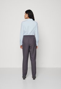 Chemise bleu clair à manches longues avec des boutons; pantalon gris à taille élastique; la vue de dos montre un tissu lisse et une coupe ajustée.