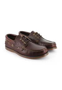 Mocasines de cuero marrón con textura suave, punta redonda, costuras en contraste, diseño con cordones y detalles en dorado.