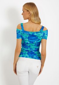 Blå og grøn blomsteret off-the-shoulder top med ruchet tekstur, korte ærmer og bred firkantet udskæring, parret med hvide bukser.