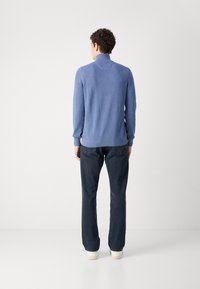 Blauer Strickpullover mit hohem Kragen, langen Ärmeln und gerippten Bündchen, kombiniert mit dunklen Jeans und hellen Sneakern.