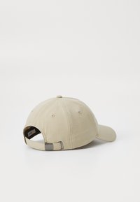 Beige textured cap with a curved brim, adjustable strap, and metal hardware. Rear view shows ventilation holes and top button detail.