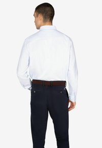 Camisa de manga larga a rayas azul claro con cuello, combinada con pantalones oscuros y un cinturón marrón. Costuras visibles y detalles de botones en las mangas.
