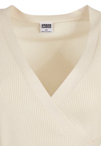 Krämmfärgad ribbad wrap-top med V-ringning. Har en mjuk textur och subtila sömmar. Märket står "Urban Classics," storlek XS.