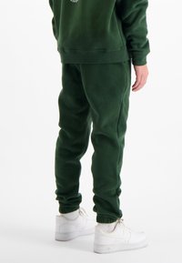 Groene fleece joggingbroeken met elastische manchetten, schuine zijzakken en een relaxte pasvorm, gecombineerd met witte sneakers. Eenvoudig en functioneel ontwerp.