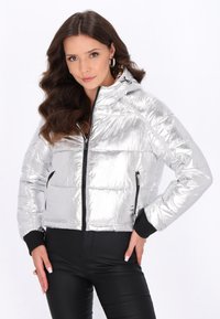 Giacca puffer argentata con finitura lucida, chiusura frontale con zip, tasche laterali e dettagli neri ai polsini e all'orlo. Design con cappuccio.