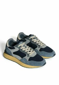 Une paire de baskets grises et bleu marine avec des lacets beiges et une semelle jaune, présentée sur un fond blanc.
