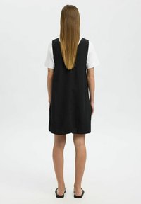 Zwarte linnen jurk met een losse pasvorm, voorzien van brede schouderbanden, een ronde halslijn en zijsplitsingen, gecombineerd met een wit shirt eronder.
