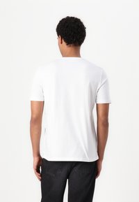 Hvid kortærmet t-shirt i bomuldsstof, med rund hals og lige kant, vist fra ryggen med et glat, rent design.