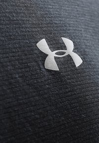 Gray textured fabric with a prominent white Under Armour logo featuring rounded edges, located on the center of the material.