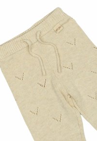 Pantalons en tricot beige avec une taille à cordon de serrage, présentant un motif texturé de petits trous en forme de V. Étiquette visible à la taille.