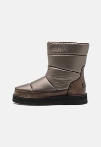 Gepolsterter brauner Knöchelstiefel mit einem eleganten Design, glänzendem Textil-Obermaterial, kontrastierender dunkler Sohle und genähten Details entlang der Kanten.