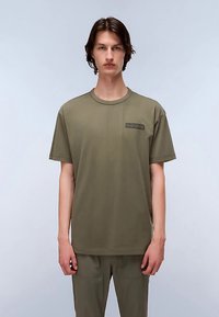 Maglietta verde oliva a maniche corte in cotone, con scollo rotondo e una toppa rettangolare nera con la scritta "NAPAPIJRI".