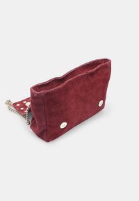 Borsa a mano in suede bordeaux con accessori in oro e tracolla a catena, dotata di un interno a pois e di una forma minimalista e strutturata.