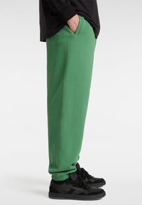 Groene sweatpants met zijzakken, elastische manchetten en een zachte textuur, gecombineerd met zwarte sneakers met zwarte en grijze accenten.
