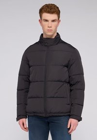 Svart vadderad jacka med hög krage, med horisontellt quiltade sektioner, dragkedja framtill och sidofickor. Mjuk, slät textur.