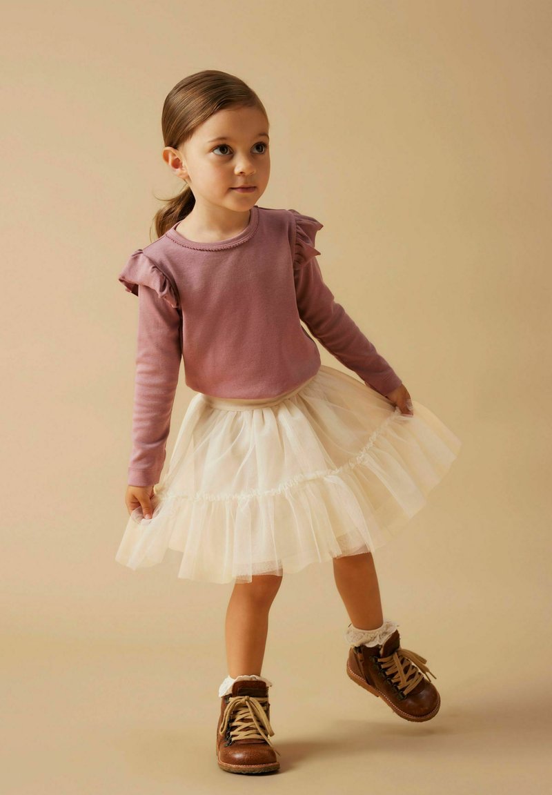 Svijetlopurple dugi rukav majica s naborom, u paru s bijelom tila suknjom i smešnim čizmama sa čipkastim manžetama.