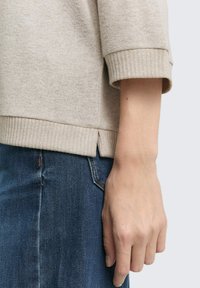 Maglione beige a maglia con orlo e dettagli a costine, abbinato a jeans in denim scuro. Fessura laterale sull'orlo inferiore per un tocco di design in più.