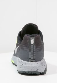 Chaussure de course Nike avec une empeigne en mesh noir, des accents jaune fluo, une semelle intermédiaire grise texturée avec un motif tacheté et un talon à motif.