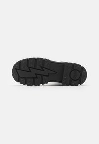 Suela de zapato de goma negra con un patrón estriado, que presenta un diseño de rayo en el centro y elementos adicionales de tracción.