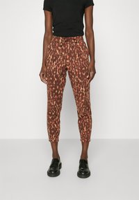 Brown pants with a red and yellow abstract pattern, featuring an elastic waistband and drawstring. Cut slim with ankle-length hem.