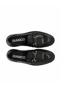 Mocasines de cuero negro con detalle de hebilla metálica, puntera redonda, suela texturizada y marca embellecida en la planta.