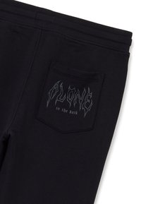 Schwarze Jogginghosen mit einem dehnbaren Bund, ausgestattet mit einer Gesäßtasche und einem grafischen Textdesign, das "ALONE in the dark" in Silber zeigt.