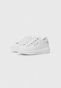 White leather sneakers with a flat sole, featuring a rounded toe, five eyelets, and embossed brand detail on the side.