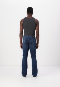 Mørkegrå ribbet tanktop kombinert med blå flagrende jeans av denim. Jeansene har baklommer med dekorative sømmer og en svart merkelapp.