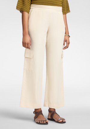 Beige Cargohose mit weitem Bein und seitlichen Taschen, kombiniert mit braunen Sandalen mit Riemen und grünem, strukturiertem Kurzarmtop.