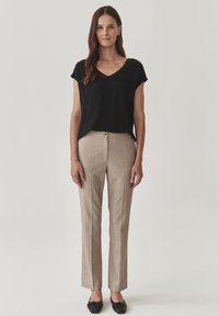 Haut noir à col en V, pantalon beige à rayures et chaussures plates noires. Le pantalon présente un bouton à l'avant et un design ajusté.