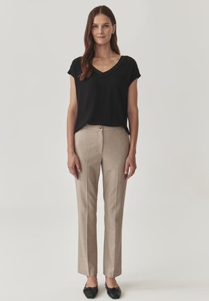 Haut noir à col en V, pantalon beige à rayures et chaussures plates noires. Le pantalon présente un bouton à l'avant et un design ajusté.