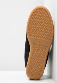 Chaussure en daim noir avec une semelle en caoutchouc gomme texturée. Présente un bout arrondi et des accents de couture subtils. Taille 37 indiquée sur la semelle.