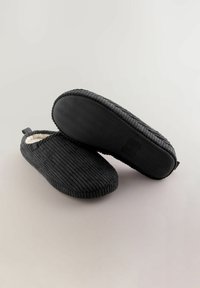 Black corduroy slippers with a soft lining, rounded shape, textured surface, and a rubber sole featuring a wave pattern.