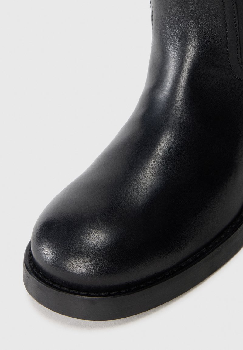 Bottine en cuir noir à bout rond, texture lisse et semelle en caoutchouc épaisse. Accents de couture minimalistes le long des bords.