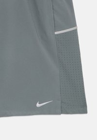 Γκρίζες αθλητικές βερμούδες με διάτρητο ύφασμα στο πλάι και μικρό λογότυπο Nike σε λευκό κοντά στο στρίφωμα.