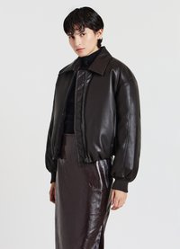 Veste bomber en cuir noir avec un devant matelassé, des manches surdimensionnées et des poignets côtelés, portée sur une jupe midi brillante marron foncé.