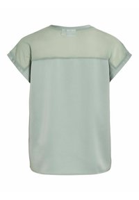 Šviesiai žalia blouse, pasižyminti permatomu nugaros paneliu, trumpomis rankovėmis ir apvaliu kaklu. Lygi tekstūra su laisvu, srauniai krentančiu siluetu.