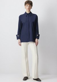 Navy button-up shirt with a collar, featuring gold star accents on cuffs, paired with white flared pants and brown shoes.