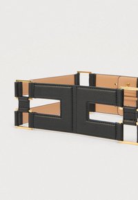 Μαύρη φαρδιά δερμάτινη ζώνη με χρυσές ορθογώνιες μεταλλικές λεπτομέρειες και γεωμετρικό σχέδιο με κοψίματα σε μπεζ φόντο.