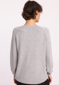 Jasnoszary sweter wykonany z miękkiego materiału, z okrągłym dekoltem, długimi rękawami raglanowymi oraz ściągaczami na mankietach i u dołu. Gładka faktura z minimalnymi detalami.