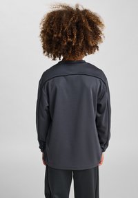 Mörkgrå långärmad träningsskjorta med rund hals, strukturerad tyg och kontrasterande sömdetaljer, bärs med matchande byxor.