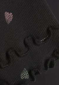 La tela de canalé negra presenta pequeños corazones en rosa y verde, con un borde texturizado y ondulado que acentúa la abertura.