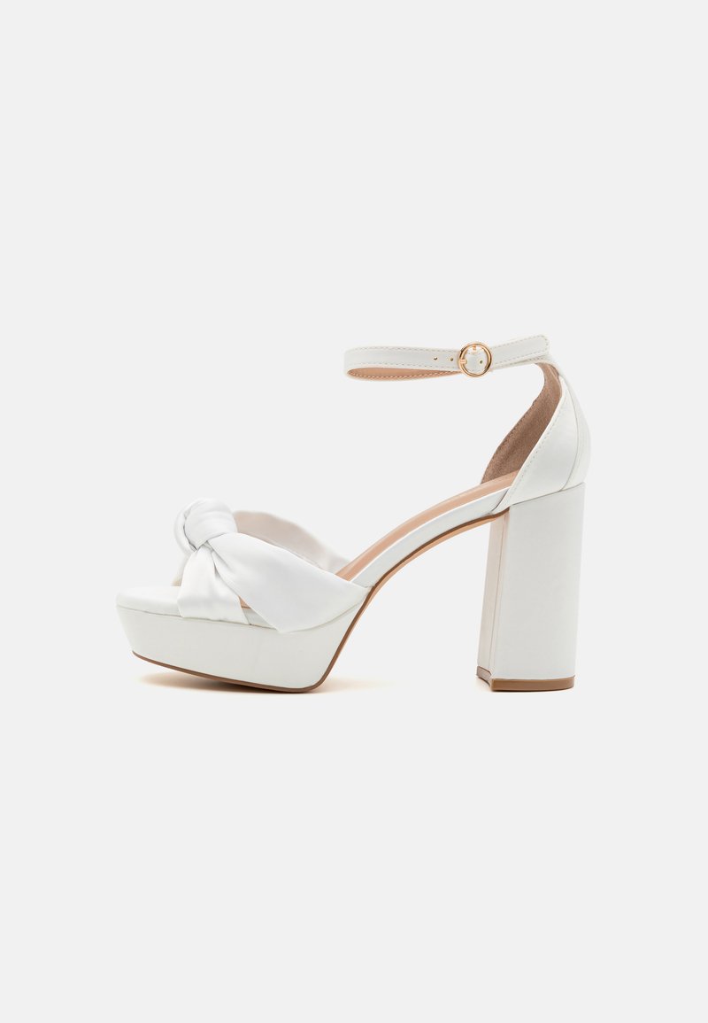 White high-heel sandals with a platform and chunky block heel, featuring a knotted fabric detail on the front and an adjustable ankle strap.