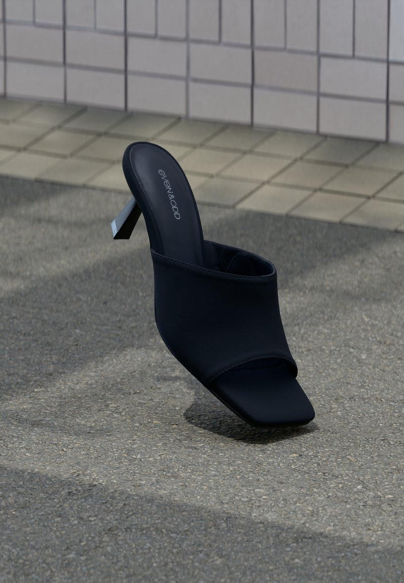 Μαύρο mule ανοιχτής μύτης με χοντρό τακούνι και τετράγωνη μύτη, με την επωνυμία «EVEN&ODD», τοποθετημένο σε γκρι πλακόστρωτο κοντά σε τοίχο με πλακάκια.