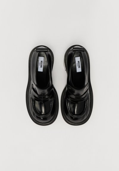 Scarpe slip-on in pelle sintetica nera con punta arrotondata, design elegante e dettagli cuciti lungo la suola. Include un logo discreto.